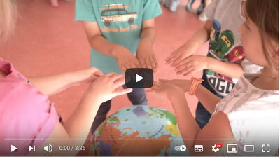 Screenshot Film Besuch FaireKITA Bollingen: Kinder halten im Kreis ihre Hände über einen Globus